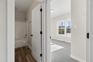 View of a bathroom with a bathtub and an adjacent bright room in Autumn Hill, featuring carpet flooring and a large window that fills Lot 19 with natural light.