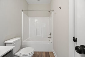 A small bathroom in Lot 19 with a bathtub, shower, and toilet, featuring Autumn Hill's signature white and gray tones complemented by elegant wooden flooring.