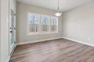 Bright, empty room with wood flooring, three large windows, and white walls lies at the heart of Lot 19 in Autumn Hill. A ceiling light fixture completes this inviting space.