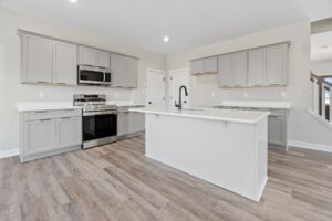 Discover the modern kitchen of Autumn Hill, tastefully designed with gray cabinets, white countertops, a center island, stainless steel appliances, and elegant wood flooring.