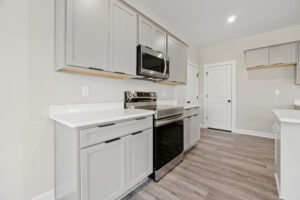 Located in Lot 19 at Autumn Hill, this modern kitchen features gray cabinets, stainless steel appliances, white countertops, and sleek hardwood floors.
