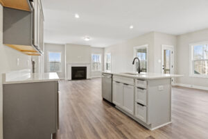 Modern kitchen and living area on Autumn Hill's Lot 19, featuring hardwood floors, gray cabinets, an island, and large windows.