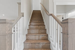 The elegant wooden staircase with white railings ascends gracefully between crisp white walls, seamlessly aligning with the modern aesthetic of Autumn Hill's Lot 19.
