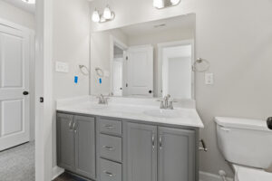 Modern bathroom with a double sink vanity, large mirror, gray cabinets, and white walls at Lot 19 in the serene Autumn Hill community.