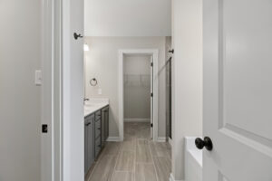 From Lot 19 at Autumn Hill, a modern bathroom unveils its elegance with a double sink vanity and tiled floor, leading seamlessly into an open walk-in closet at the back.