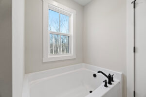 A white bathtub with sleek black fixtures sits near a window, offering a serene view of the bare trees on Autumn Hill.