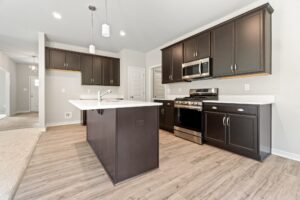 A modern kitchen with dark wood cabinets, a central island, stainless steel appliances, and wood-look flooring.
