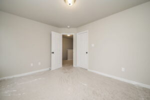 A vacant, freshly painted room with white walls, two closed white doors, a plastic sheet on the carpeted floor, and a ceiling light in the center of the room.