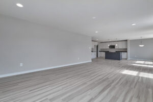 Spacious, unfurnished open-concept living area with light wood flooring, recessed lighting, and a modern kitchen featuring white cabinets, stainless steel appliances, and an island.