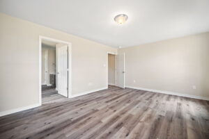 An empty room with light-colored walls, ceiling light, and wooden flooring. Two doorways are visible, leading to other areas of the house.