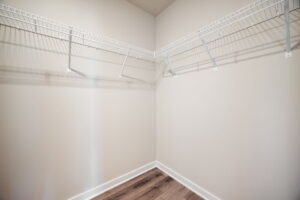 Empty walk-in closet with beige walls, white wire shelving on two sides, and a wooden floor.