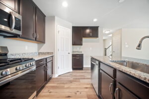 Modern kitchen with dark wood cabinets, granite countertops, stainless steel appliances, and a large island. Light wooden flooring and recessed lighting create a bright, open space.