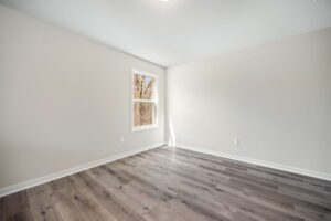 Empty room with light-colored walls, a single window with outside view, and dark wood flooring.