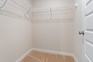 Empty walk-in closet with beige walls, brown carpet, white wire shelving, and a closed white door.