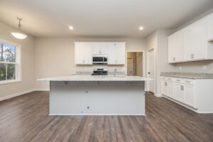 A modern kitchen with white cabinets, granite countertops, a large island, stainless steel appliances, and hardwood floors.