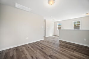 A bright room with light gray walls, multiple windows, light fixtures on the ceiling, and dark wood laminate flooring. A partial wall separates two spaces.