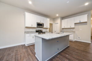 Modern kitchen with white cabinets, granite countertops, stainless steel appliances, and a large central island with a sink, set against a hardwood floor.