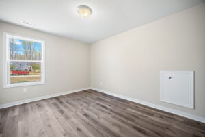 Empty room with beige walls, a single ceiling light, medium-tone wood flooring, and a window with a view of construction equipment outside.