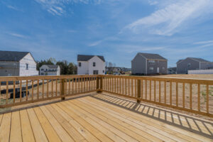 View of a newly built, empty wooden deck overlooking a residential neighborhood with several houses under construction on a clear day.
