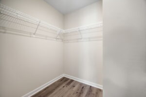 An empty walk-in closet with beige walls, white wire shelving, and a wooden floor.