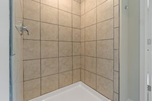 A shower area with beige tiled walls and a white base, featuring a silver showerhead.