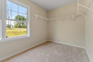 Empty walk-in closet with beige walls, carpet floor, white wire shelving, and a window with a view of trees and grass outside.