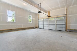 A clean, empty garage interior with unfinished drywall, two small windows, high ceilings, and a closed double garage door.