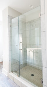 A modern shower with glass doors, tiled walls, and a light-colored floor. The shower is enclosed in a bright, clean bathroom.