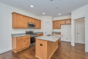 A modern kitchen with wooden cabinets, granite countertops, a center island, stainless steel microwave, and stove, with hardwood flooring and recessed lighting.
