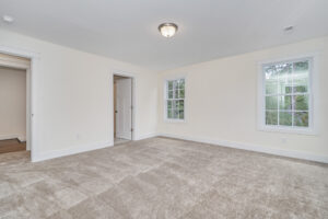 Empty room with beige carpet, off-white walls, and a ceiling light. Features two windows and two open doorways leading to other rooms.