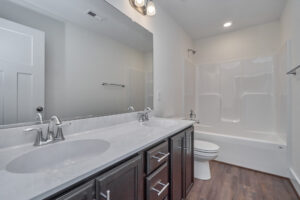 Modern bathroom with double vanity, dark wood cabinets, large mirror, dual sinks, white bathtub-shower combo, and wooden floor.