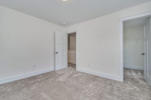An empty room with beige carpet, white walls, an open door, and an open closet door revealing shelving.