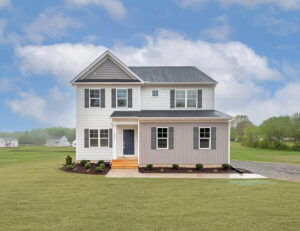A two-story house with a gray and white exterior, situated on a green lawn with a clear blue sky in the background. The house features multiple windows and a front porch.