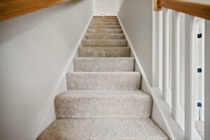 A carpeted staircase with wooden handrails elegantly leads to a bright upper floor in the charming Poplar Village of Stafford.