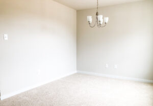 An empty room with beige carpet, off-white walls, and a ceiling-mounted light fixture with three bulbs.