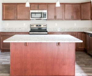 Modern kitchen with wooden cabinets, granite countertops, stainless steel appliances, and an island. Two pendant lights hang above the island.
