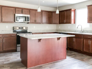 A modern kitchen with wooden cabinets, granite countertops, stainless steel appliances, an island in the center, and pendant lights overhead.