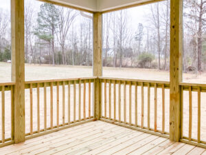 A wooden porch with railings overlooks an open field with sparse trees in the background. The sky is overcast.
