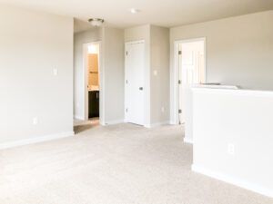 An empty carpeted room with white walls, recessed lighting, and multiple doorways leading to a bathroom and other rooms.