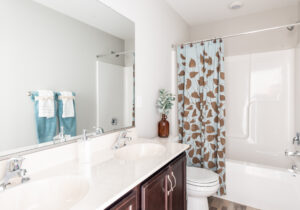 A bathroom with twin sinks, a large mirror, dark wood cabinets, a blue and brown leaf-patterned shower curtain, and white towels on the rack.