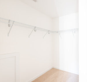 An empty walk-in closet with white walls, beige carpet, and white wire shelving on two sides.