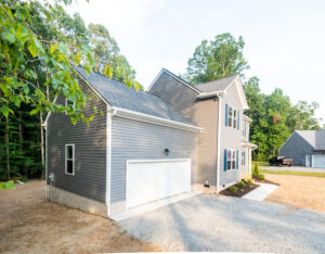Nestled in the serene Poplar Village, this gray two-story house with a two-car garage sits gracefully on a gravel driveway, surrounded by majestic trees that lend it an air of tranquility. The charming residence on Rowland blends perfectly with its picturesque surroundings.
