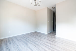 An empty room with light-colored walls and hardwood floors, featuring a hanging light fixture and an open doorway leading to another room.
