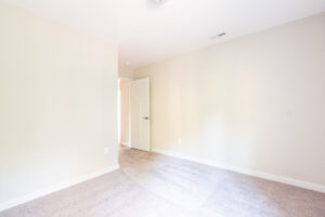 Empty room with beige walls and carpeted floor, featuring a white door slightly ajar and natural light coming through.