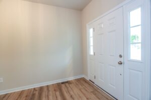 A white front door with glass panels brightens the entryway of new homes in Richmond VA with wood floors and beige walls.