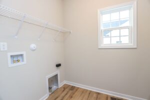 Empty laundry room with window, wall shelf, hookups, pet door, and wood-style flooring in new homes in Richmond VA.