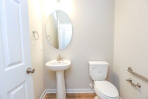 Small bathroom in new homes in Richmond VA with pedestal sink, oval mirror, toilet, and beige walls.