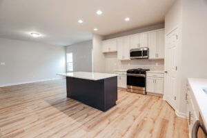 Modern kitchen in new homes in Virginia with light wood floors, white cabinets, black island, and stainless appliances.