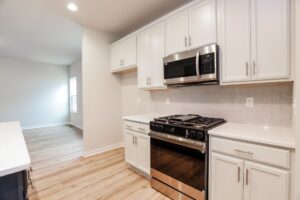 Modern kitchen in new homes in Richmond VA with stainless steel oven, white cabinets, and light wood flooring.