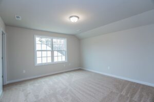 Empty, carpeted room in one of the beautiful new homes in Richmond VA, featuring beige walls and a large sunlit window.